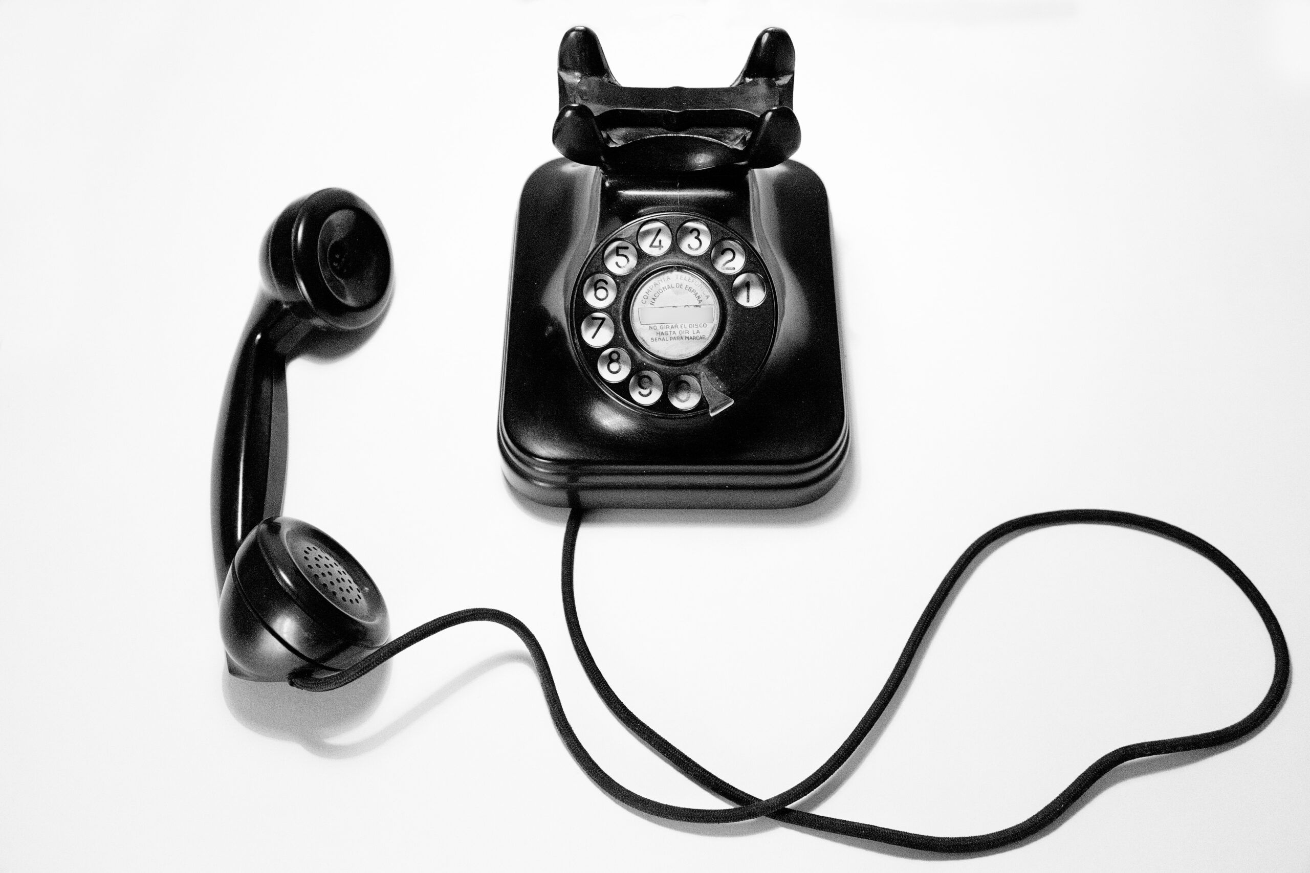A black rotary phone with the receiver off of its hook